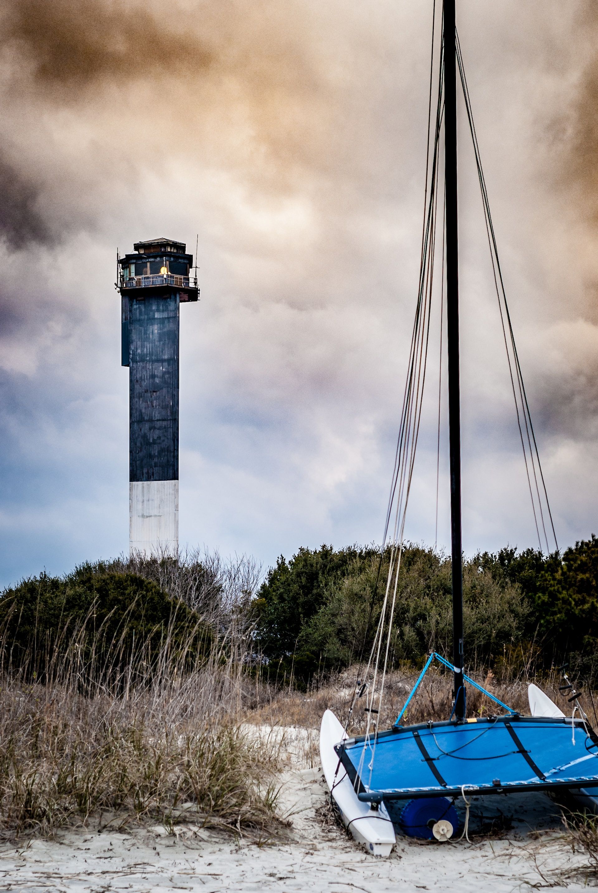 Small catamaran on the beach with Sullivan's Island lighthouse in the background