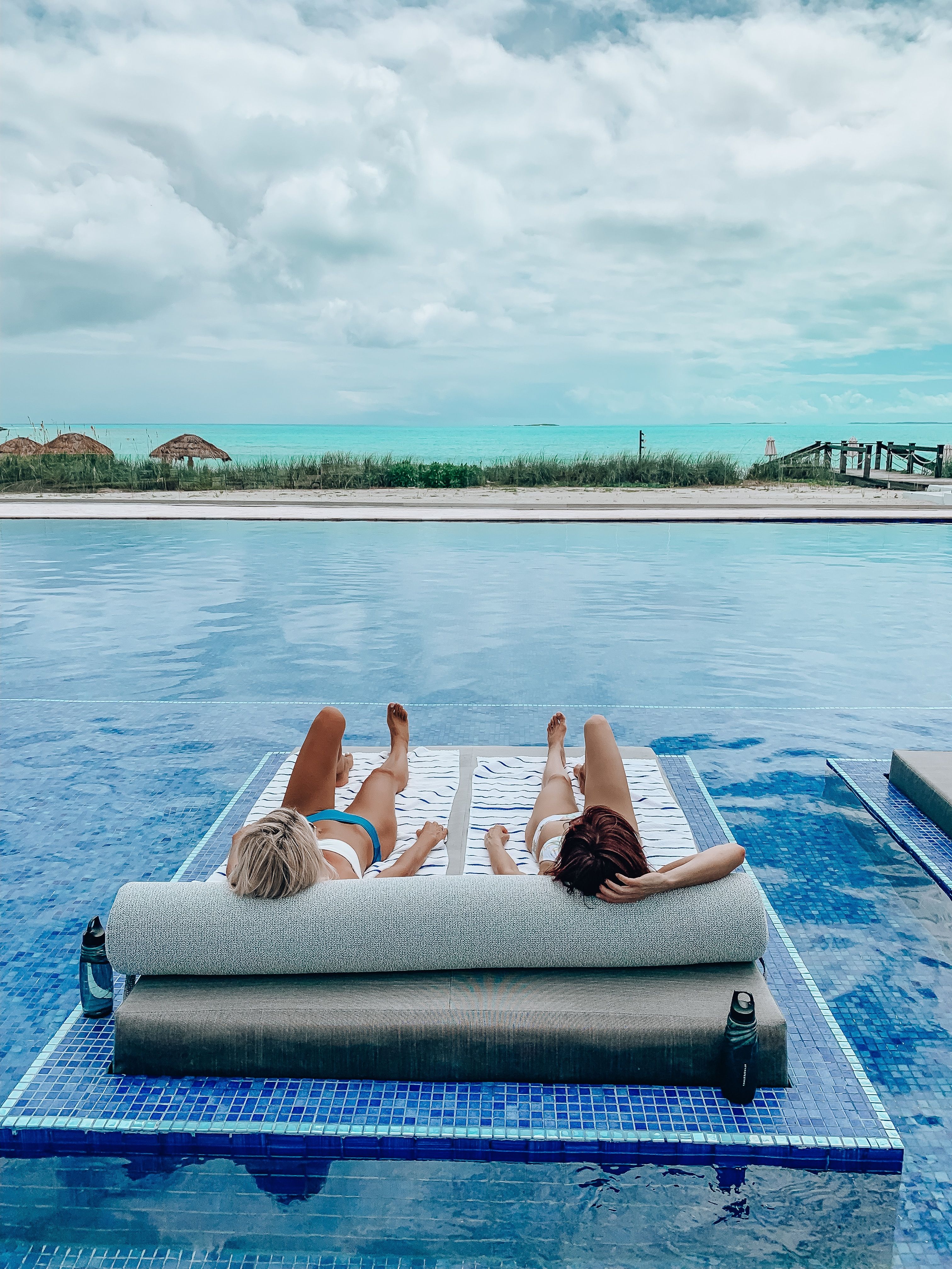 Two people lying on a blue towel at a pool 