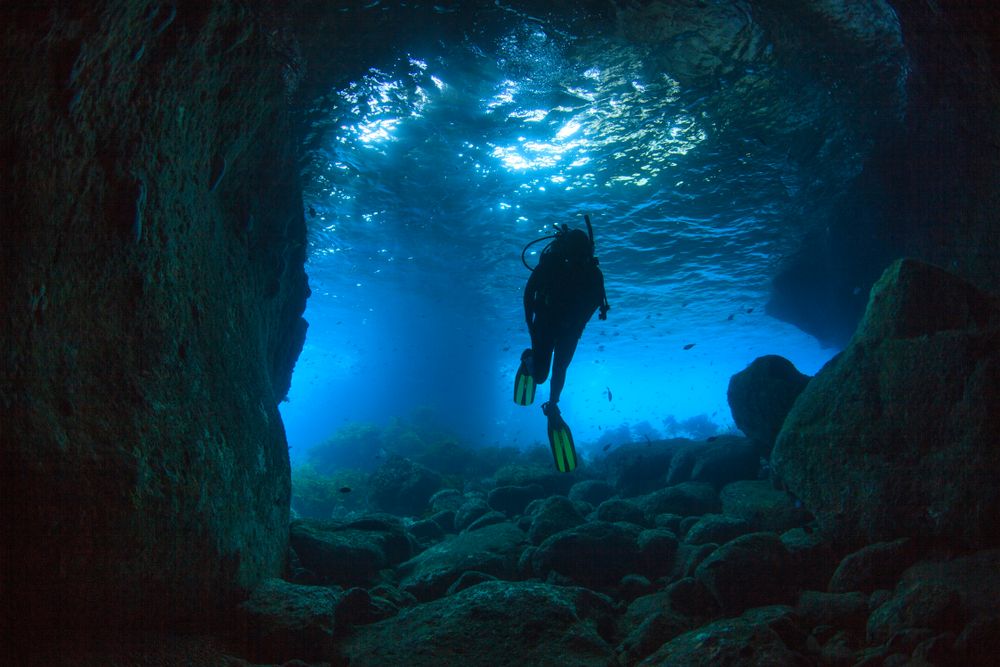 Diver going through a sea cave near Poor Knights Islands, North Island, New Zealand