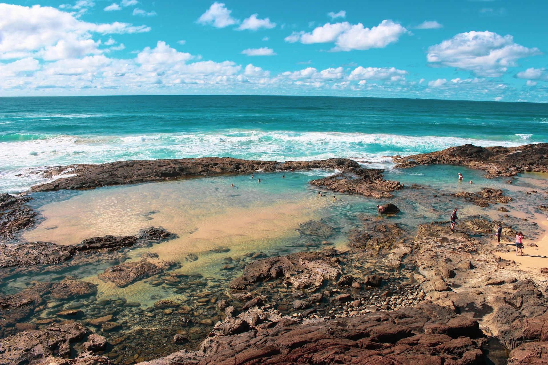 Visitors enjoying the sunny, warm weather by swimming in the Champagne Pools of Fraser Island, Australia