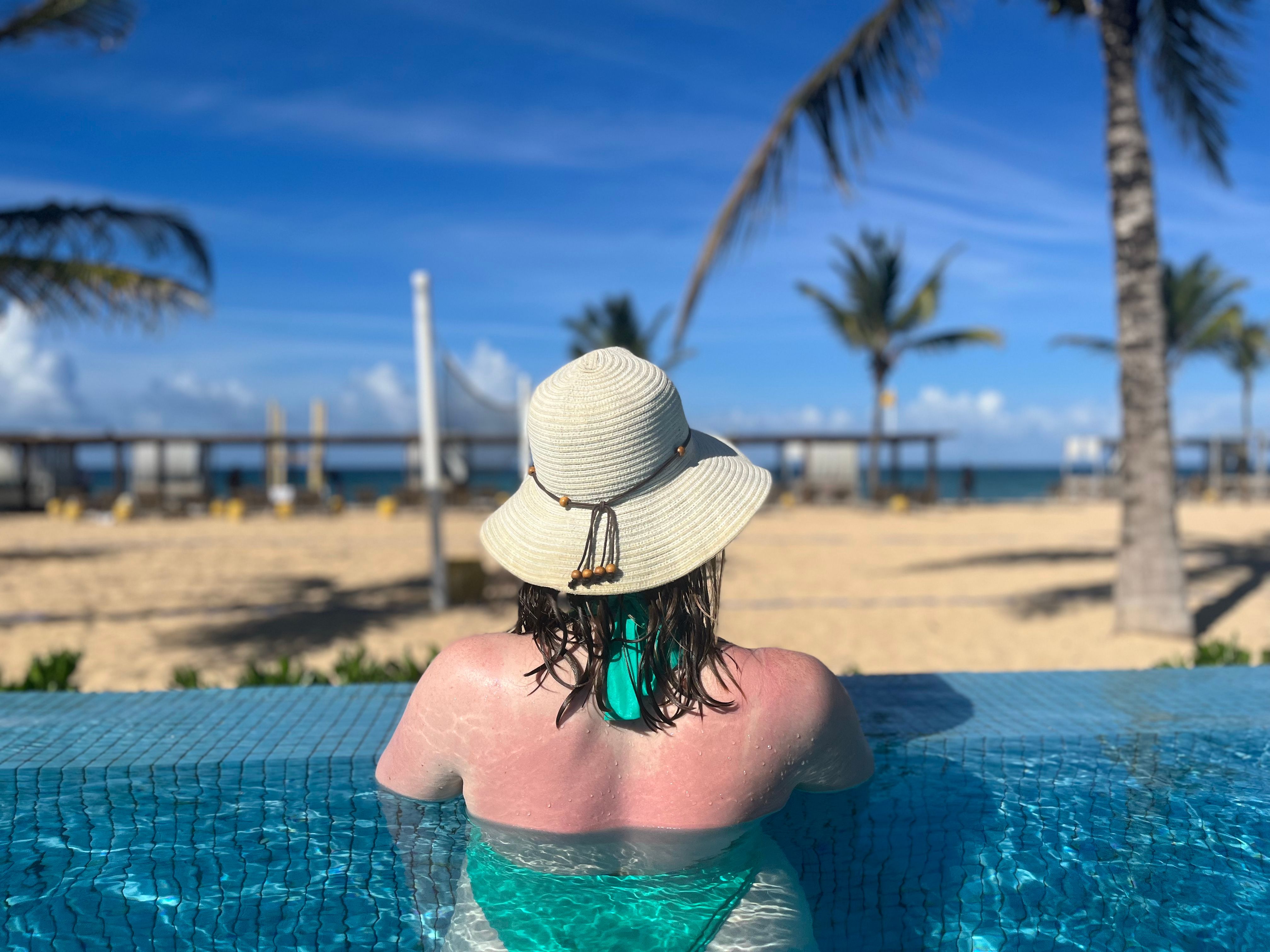 woman with hat swimming in infinity pool 