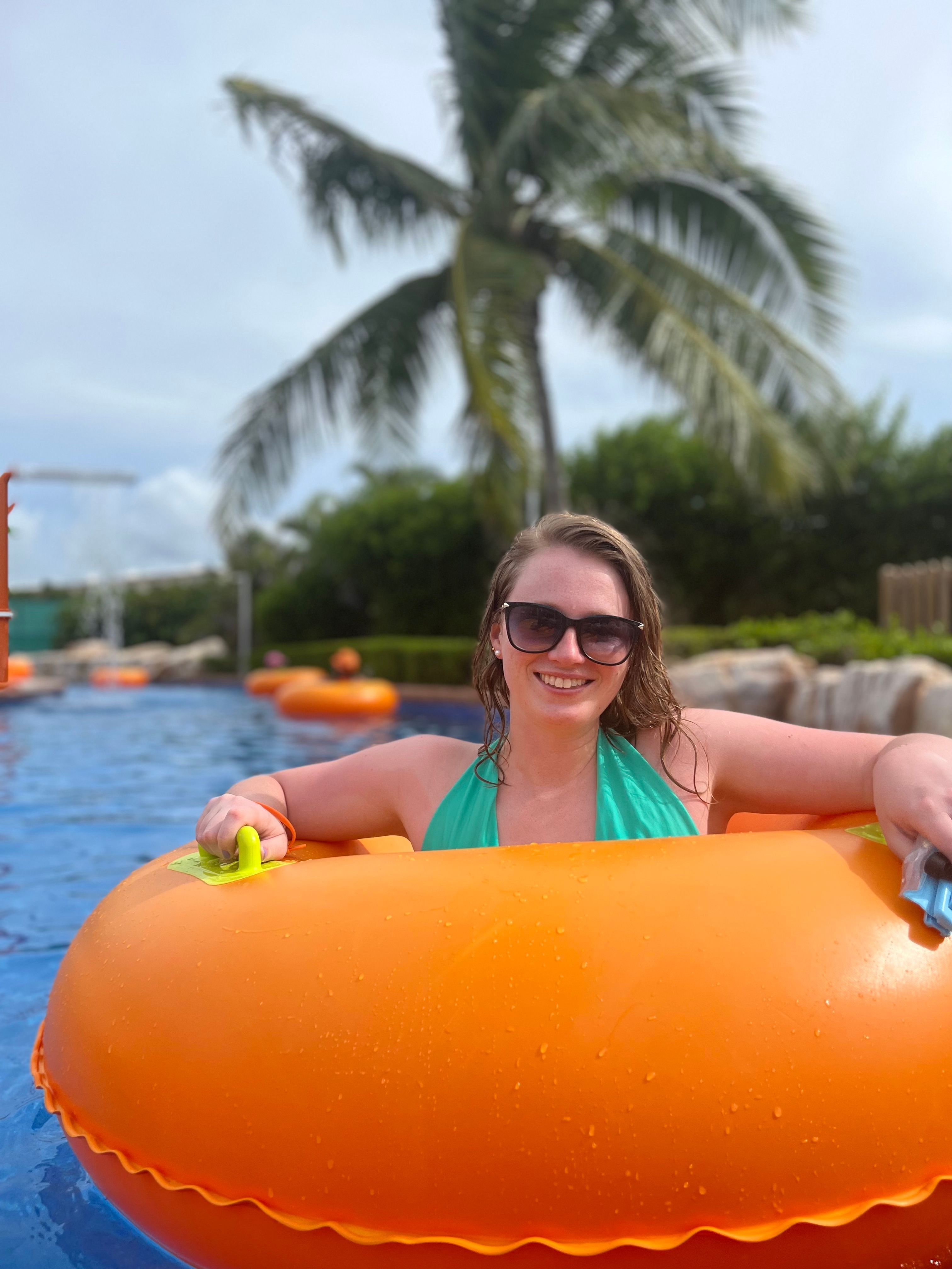 Woman floating in an orange tube on a blue river with palm trees 