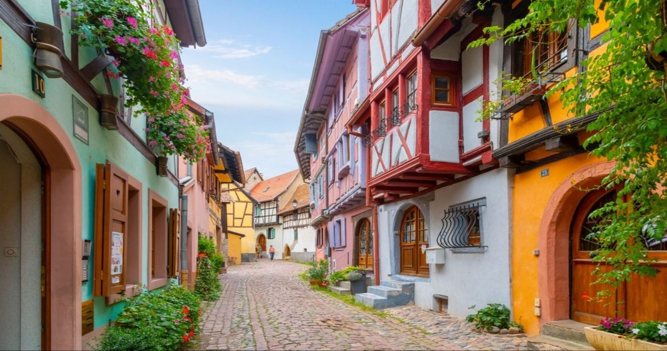 A narrow cobblestone alley with colorful half-timber buildings in the medieval Alsatian village of Eguisheim in France