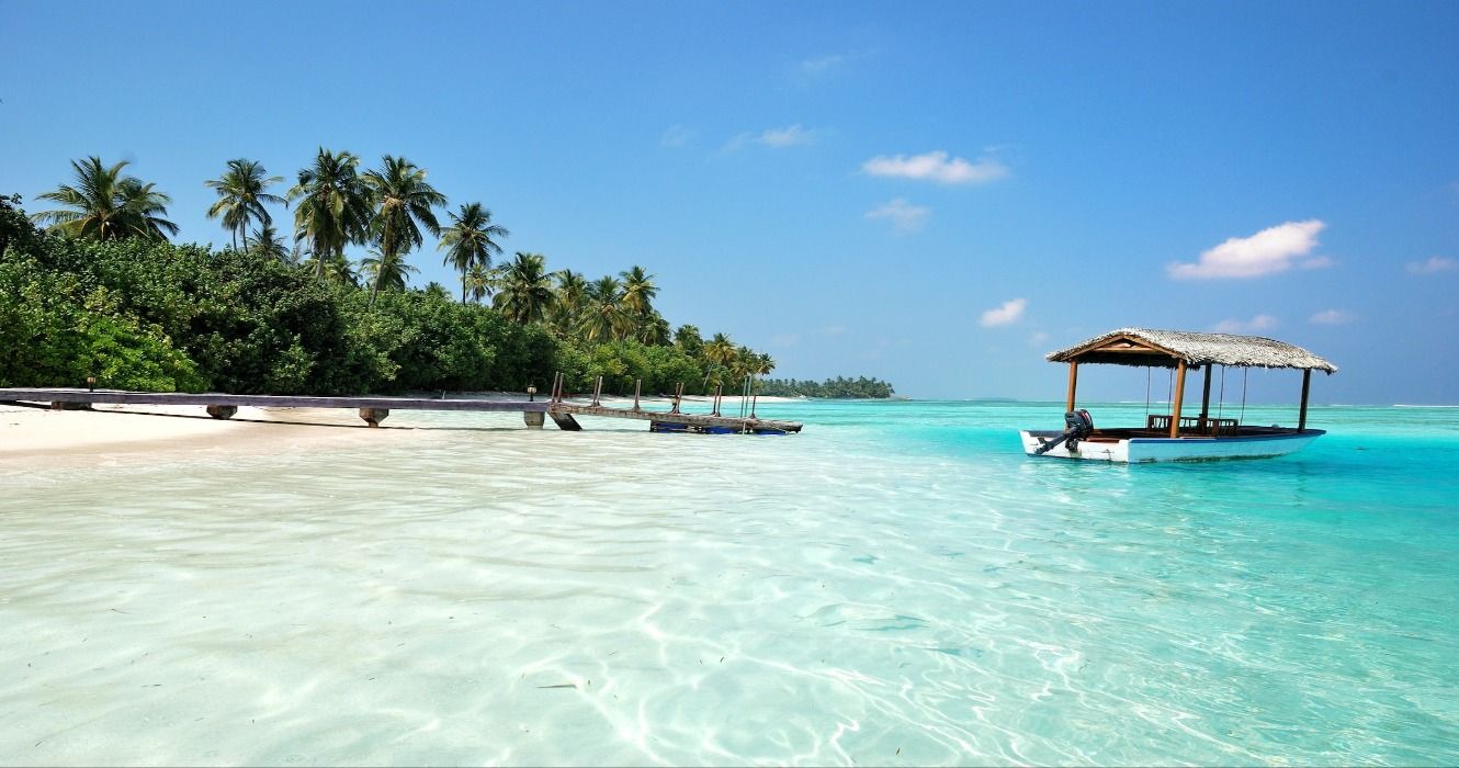 A boat in turquoise waters on a white-sand beach on the island of Medhufushi in the Maldives