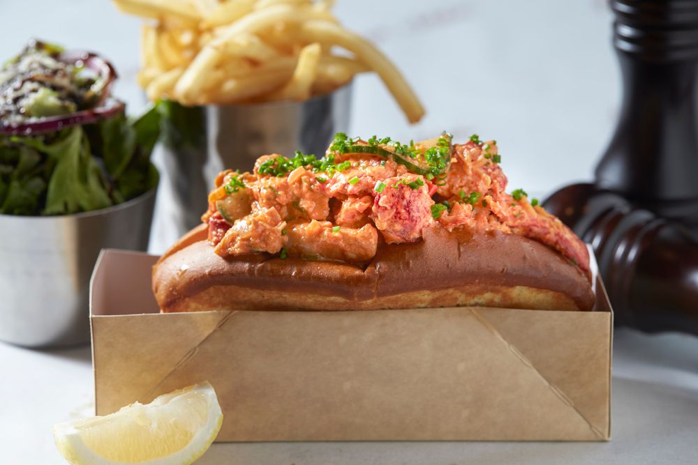 A lobster roll with a salad and fries