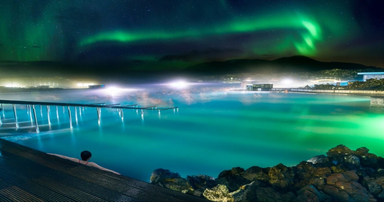 A person relaxing at Blue Lagoon at night in Iceland with the Northern Lights in the sky