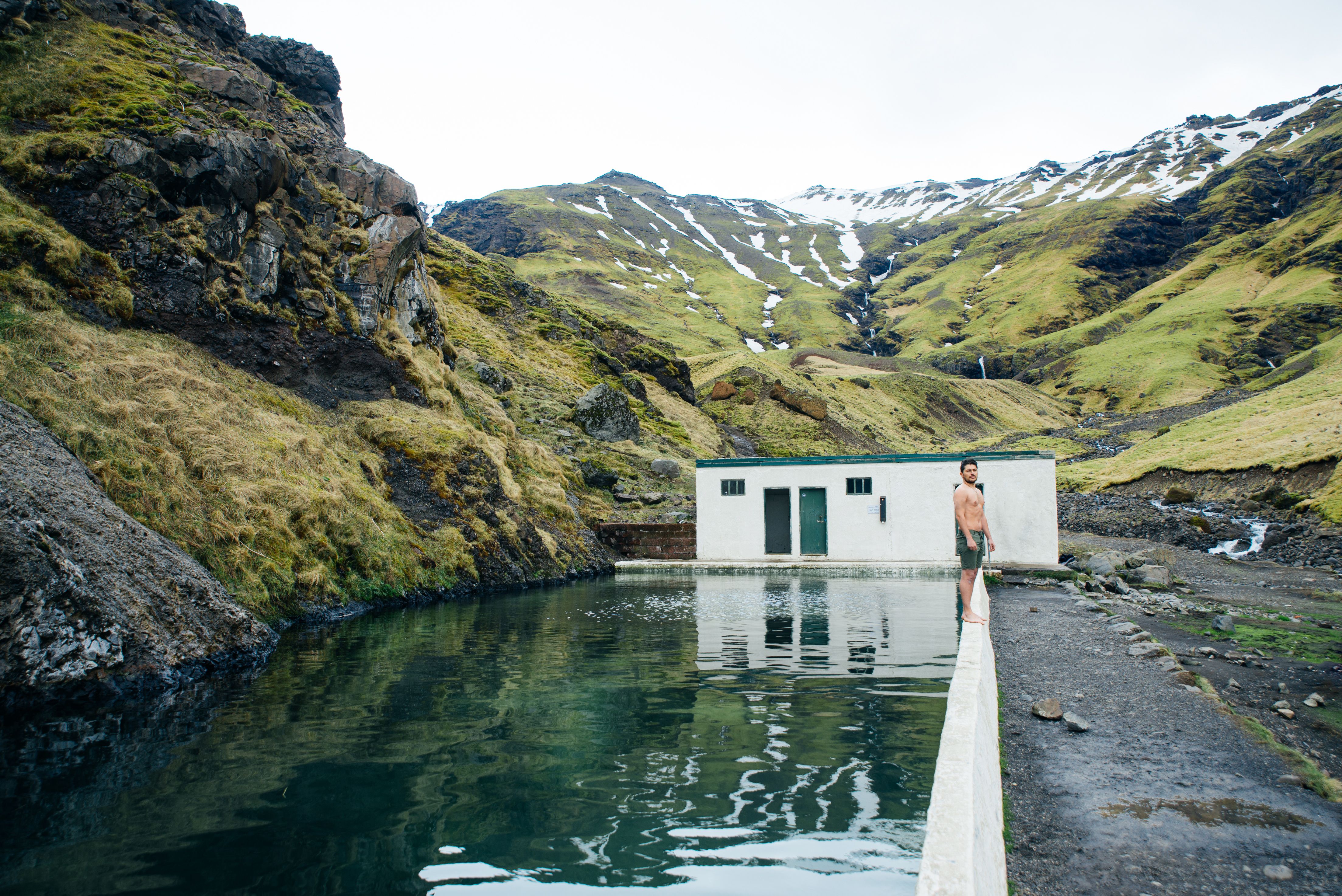 Geothermal bath amid mountain landscape with a man in swim shorts 