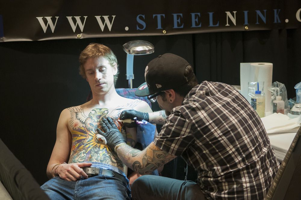 A tattoo artist working closely on a tattoo on his clients chest