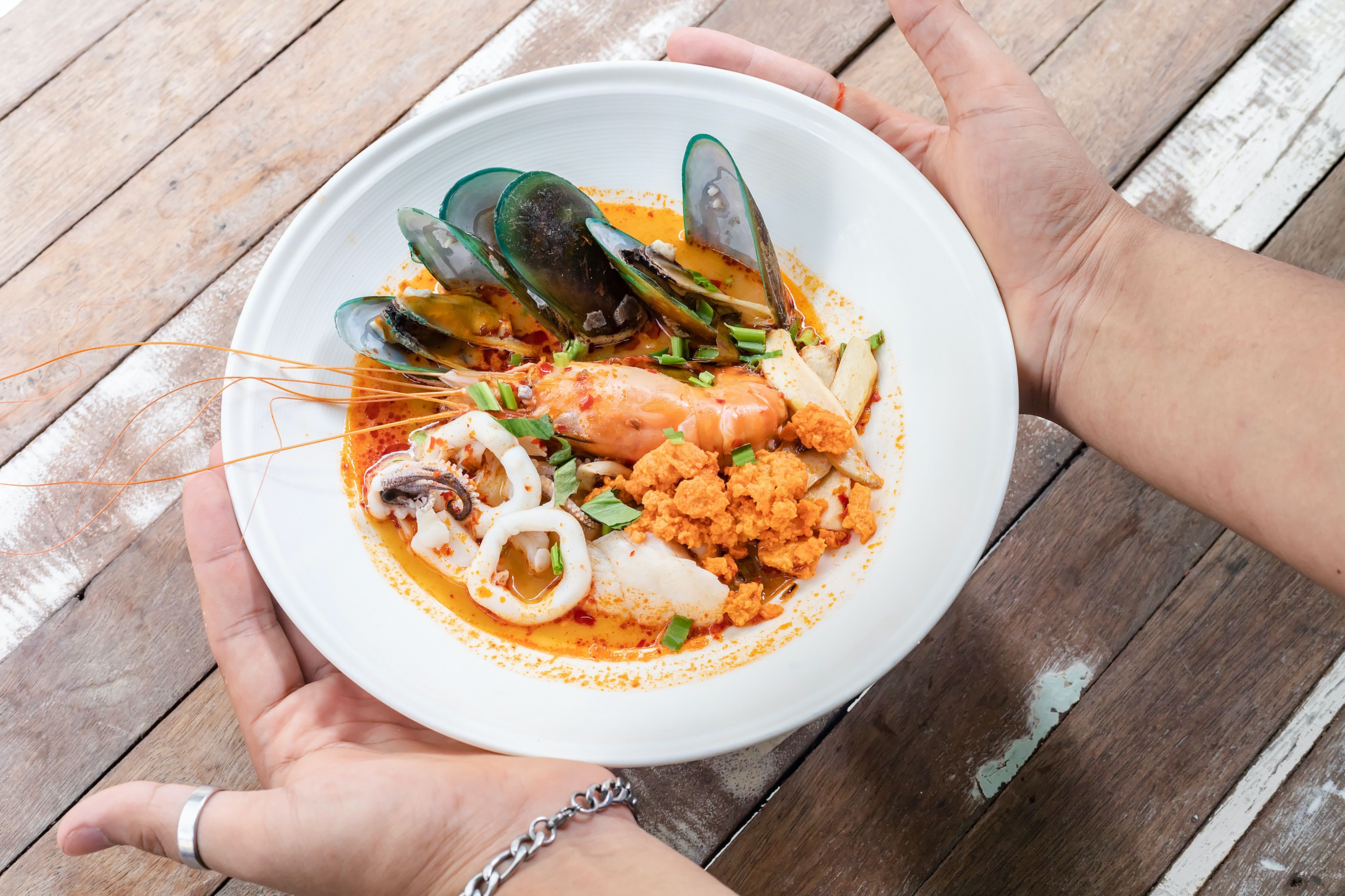 Person holding a white bowl of curry and seafobod