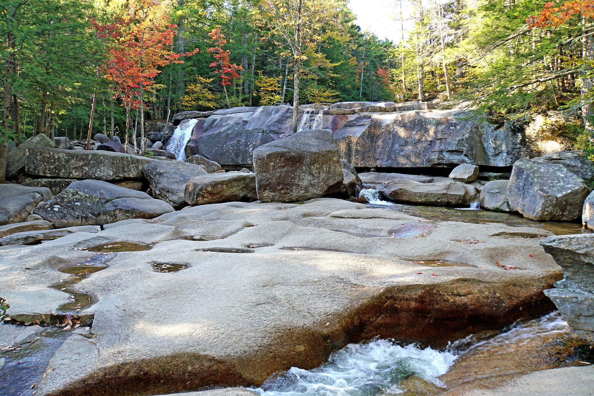 Rocky terrains of Diana's Baths with trees in the background and fall foliage in New Hampshire