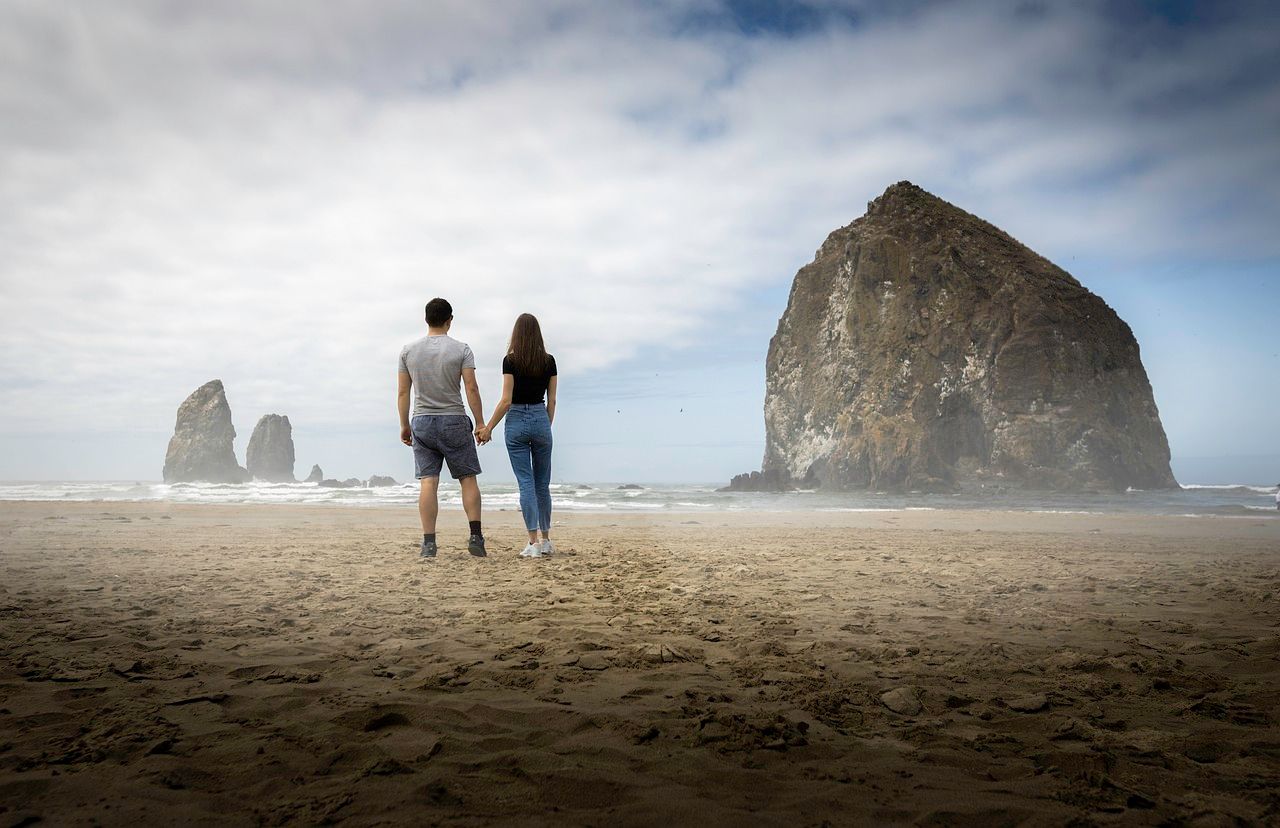 A couple holding hands on Cannon Beach while viewing the Haystack Rock, Oregon 