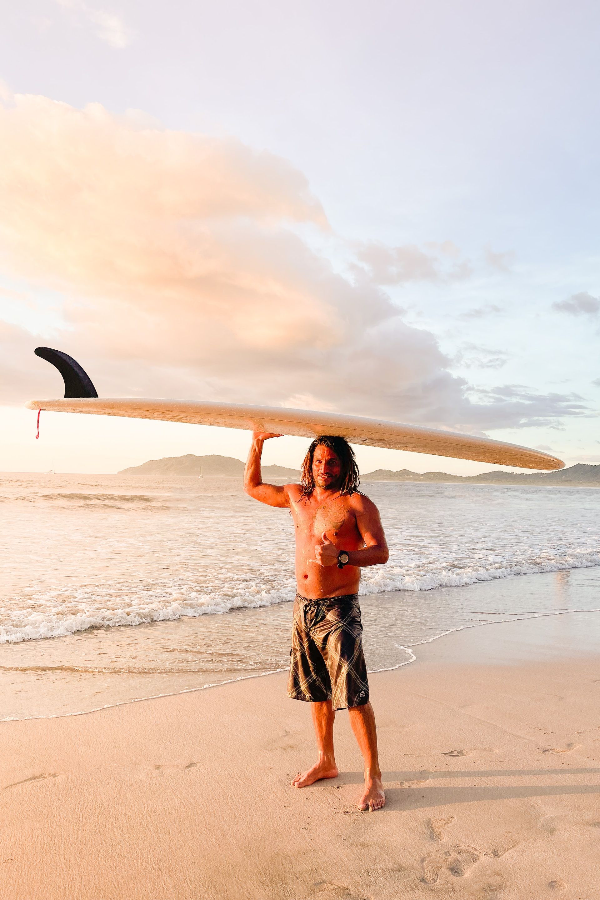 Surfer standing on the beach in Tamarindo giving a shaka while holding a longboard