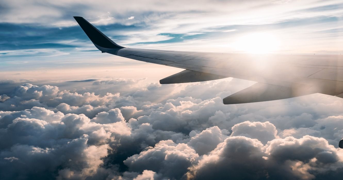 An airplane wing seen from the plane window during a flight above the clouds