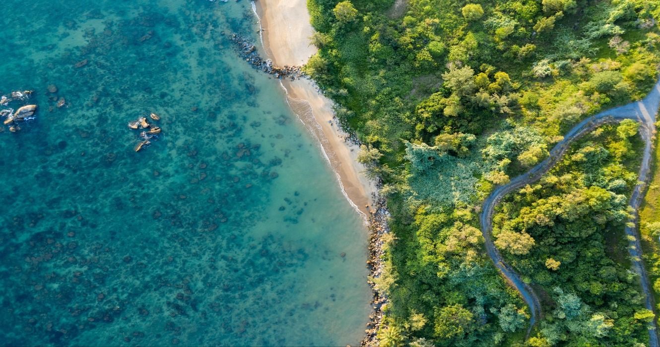 An aerial view of a white-sand beach, turquoise ocean, and a green tropical forest in Danang, Vietnam