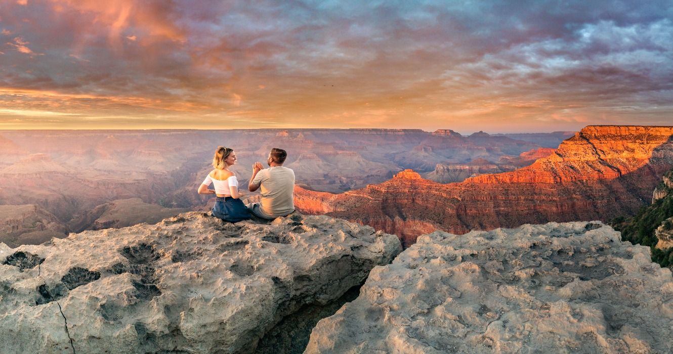 A couple sitting on the edge of the Grand Canyon rim at sunset, Arizona, USA