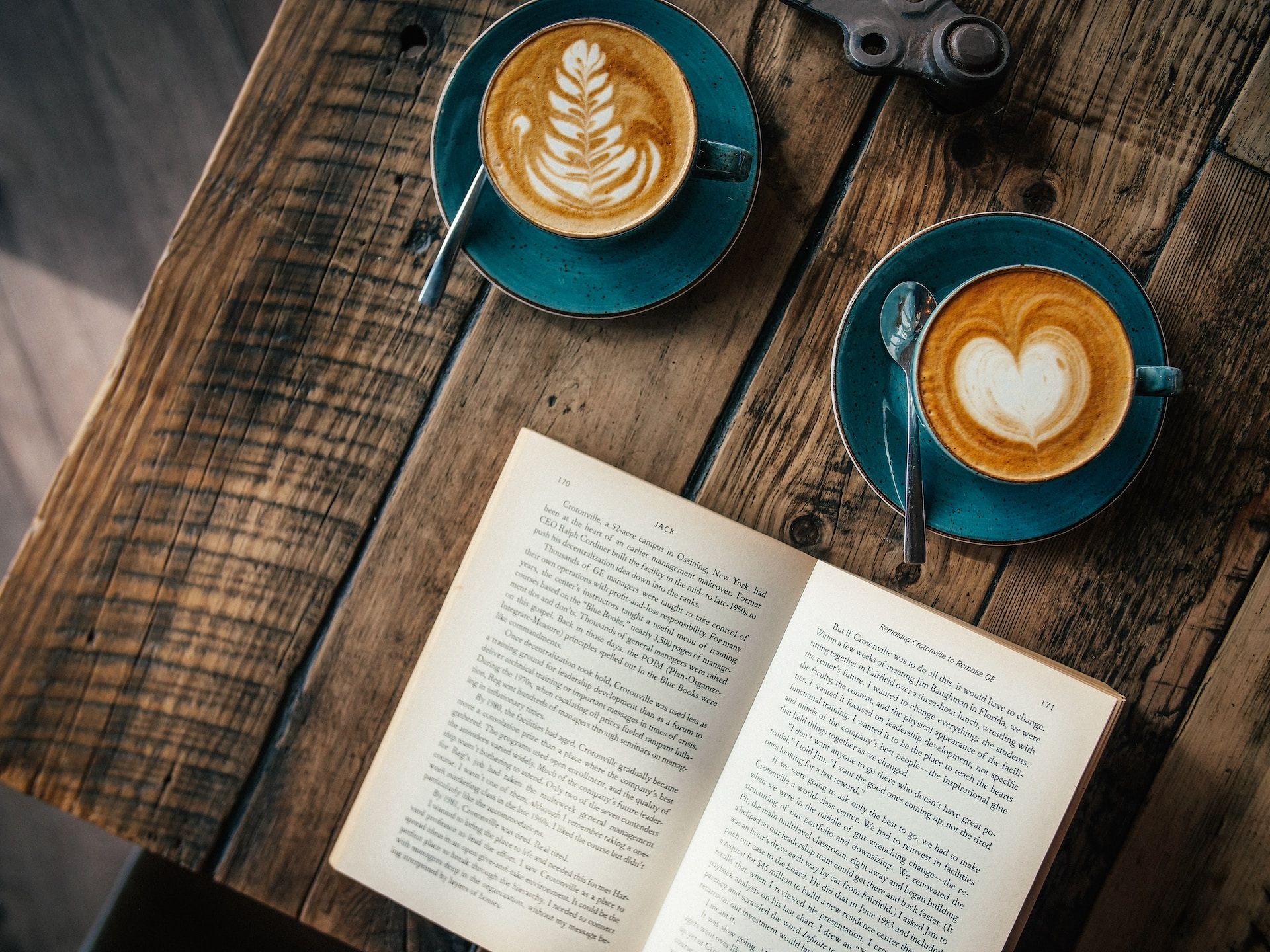 Two well-made coffees sat ahead of an open book on a wooden table