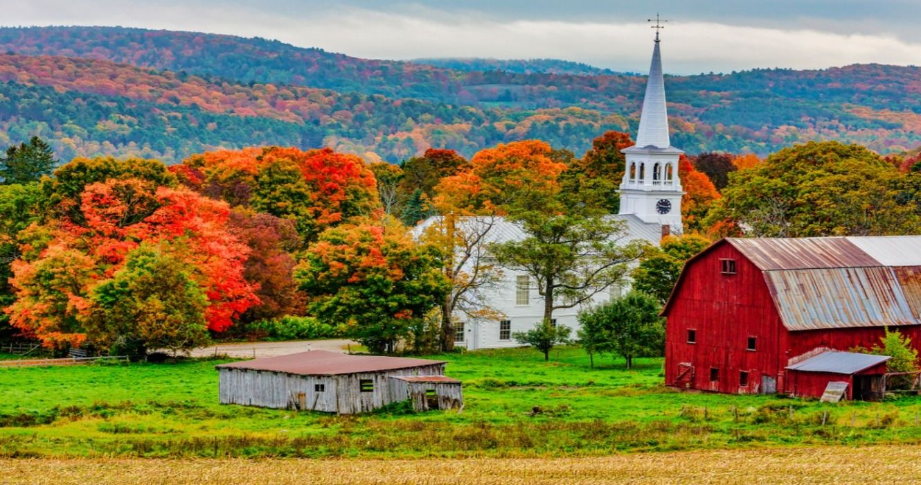 Red barn and a church next to a harvested cornfield surrounded by fall foliage colors in the autumn, Woodstock, Vermont, USA