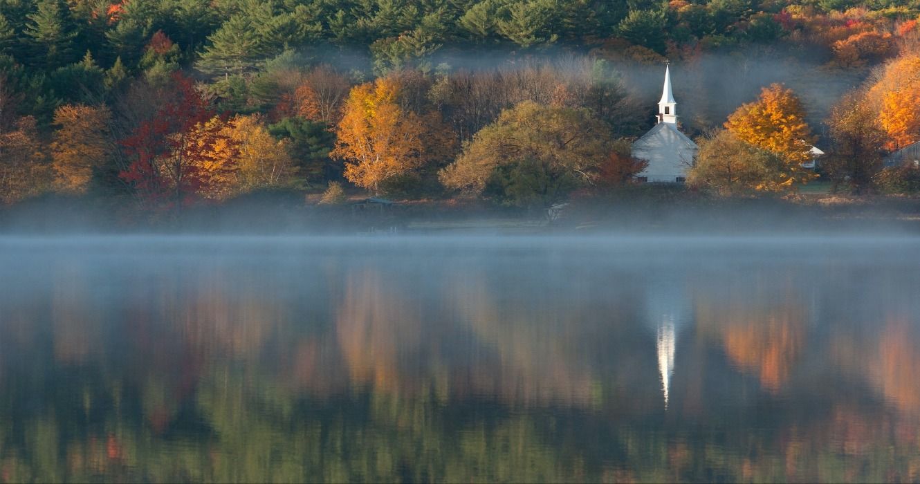 Fall foliage in the autumn around the Little White Church in Eaton, New Hampshire, seen from Crystal Lake, New England, USA