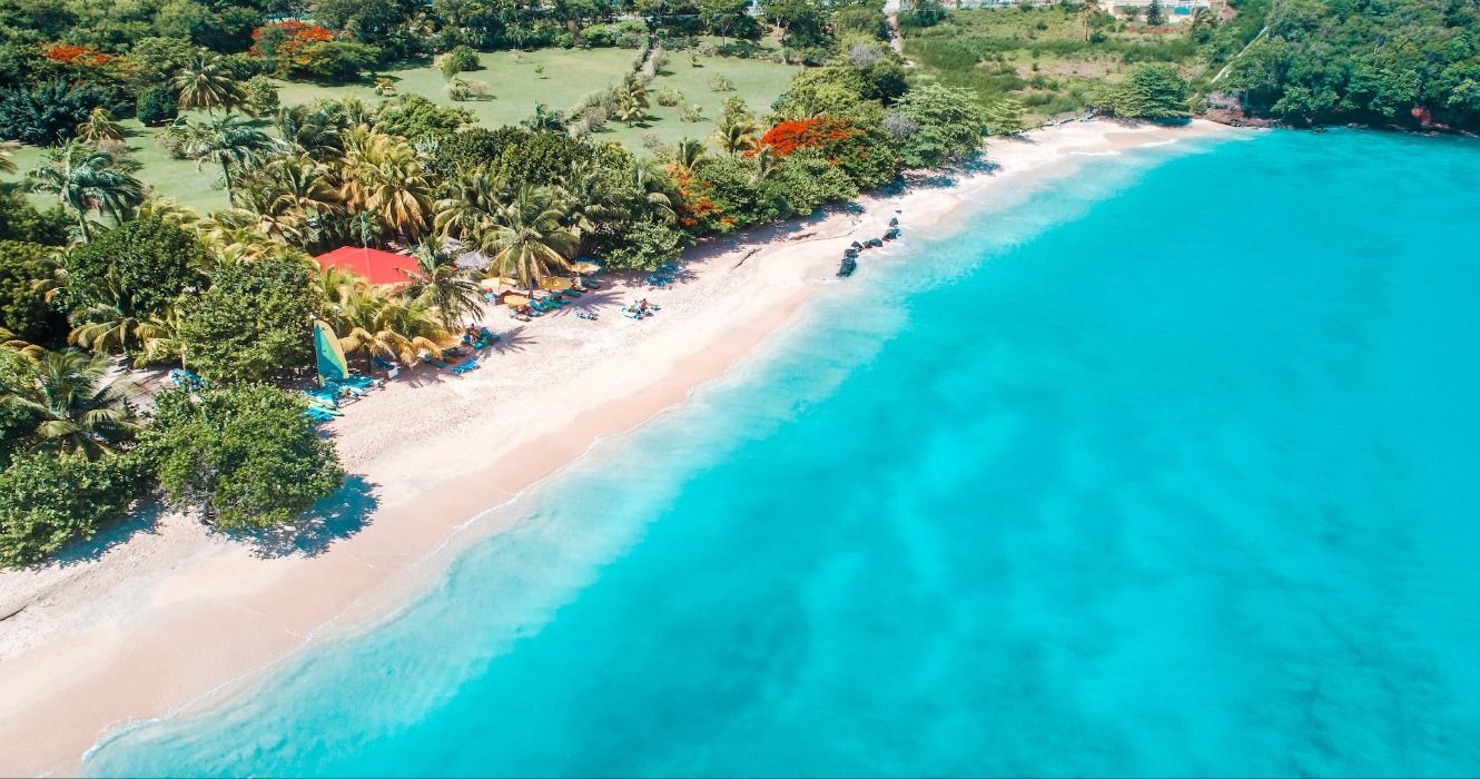 An aerial view of lush green tropical vegetation, white sand, and turquoise ocean at Grand Anse Beach, Morne Rouge, Grenada, Caribbean