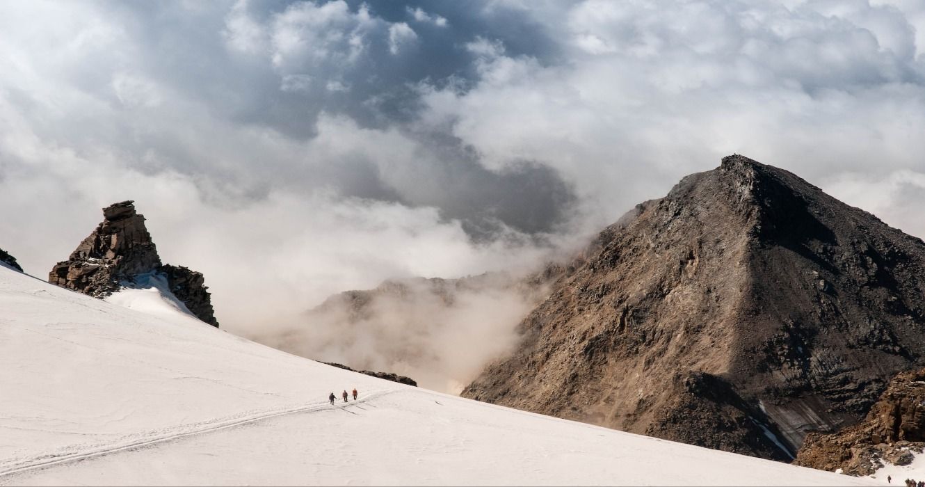 People walking on snow with a mountain in the distance while hiking in Gran Paradiso National Park, Italy