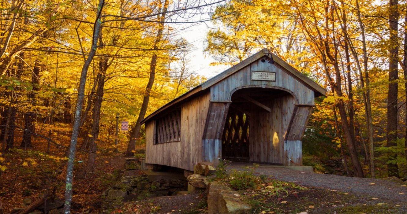 A scenic covered bridge in a rural forest in New Hampshire, New England, USA, surrouded by fall foliage in the autumn
