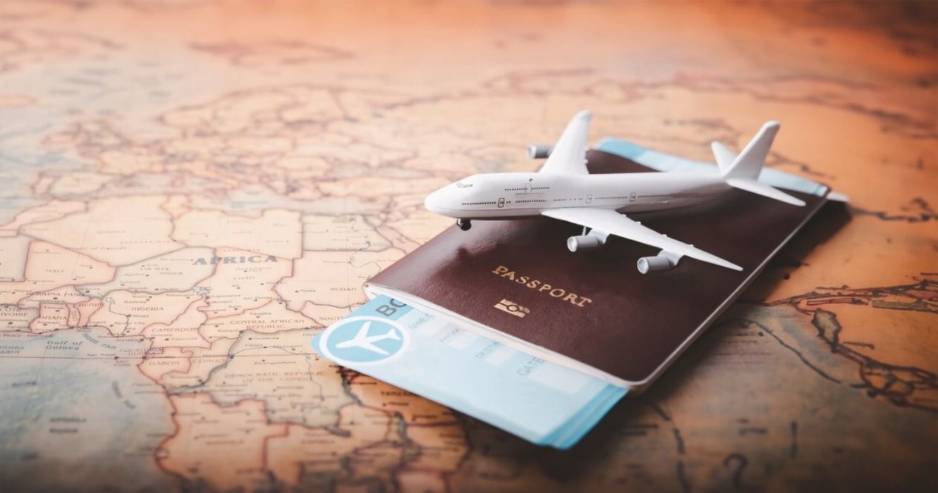 A small model airplane figurine on top of a passport with plane tickets and a global map atlas