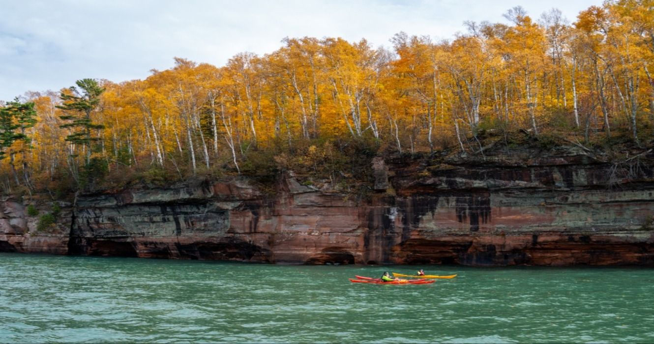 People kayaking through the sea caves below fall foliage in the autumn at Apostle Islands National Lakeshore in Wisconsin, USA