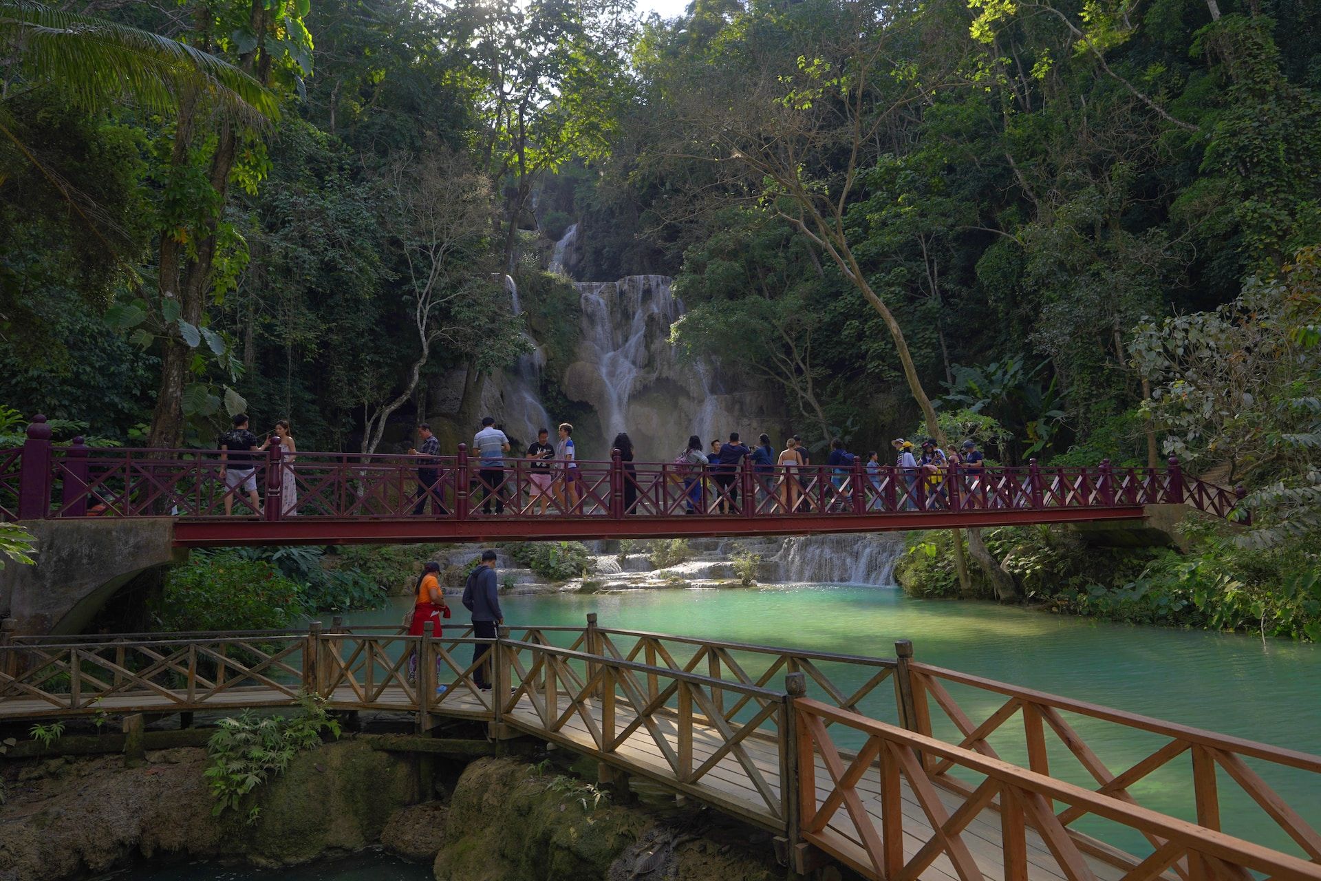 Tourists on a bridge admiring the Kuang Si Falls, a top attraction in Luang Prabang, Laos