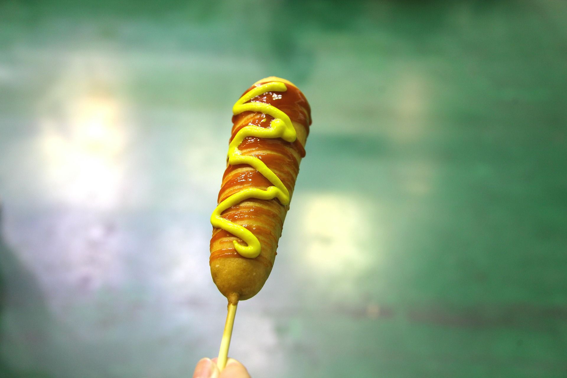 Corn dog on a stick with ketchup and mustard