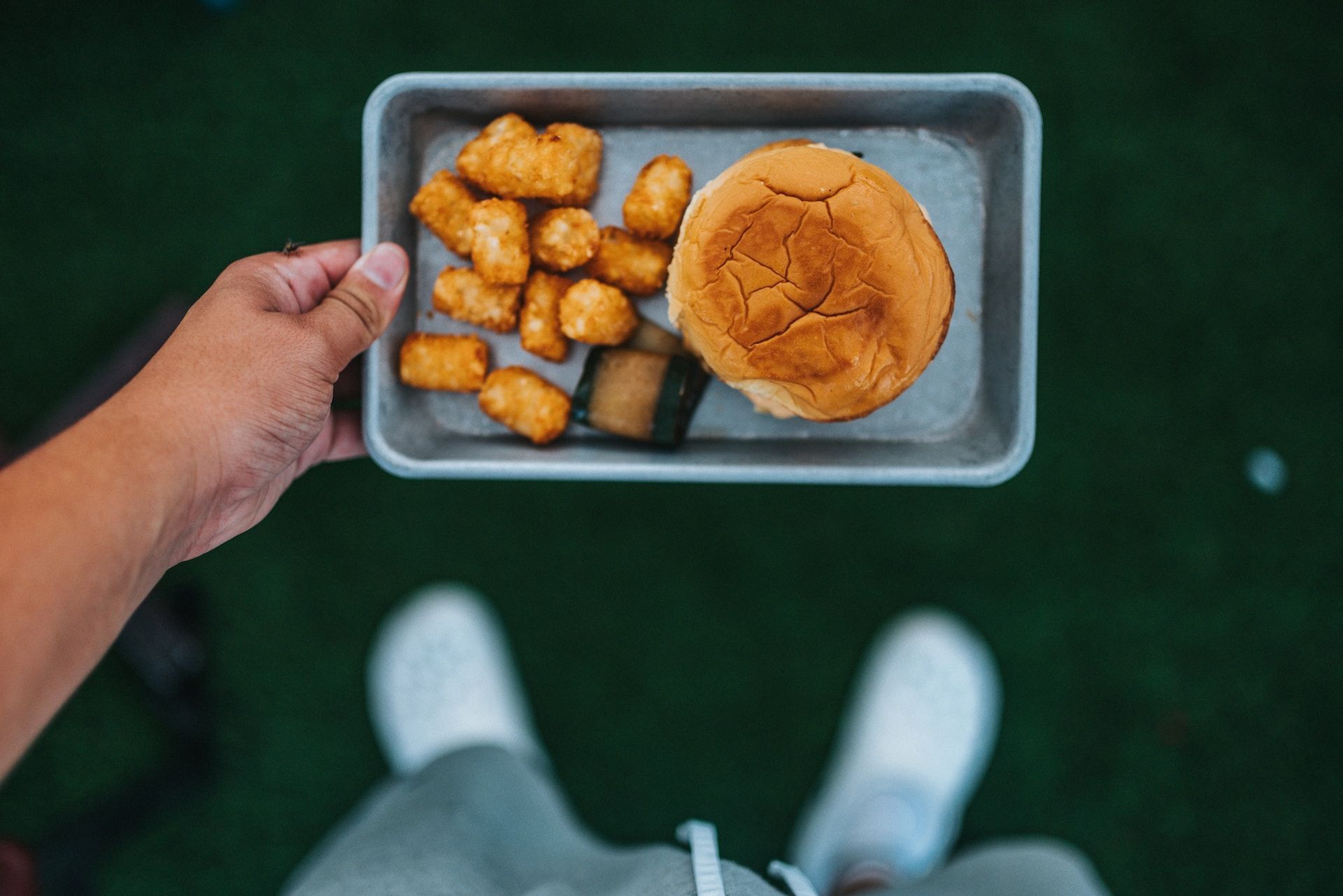 Person holding a tray with a hamburger and a side of tots