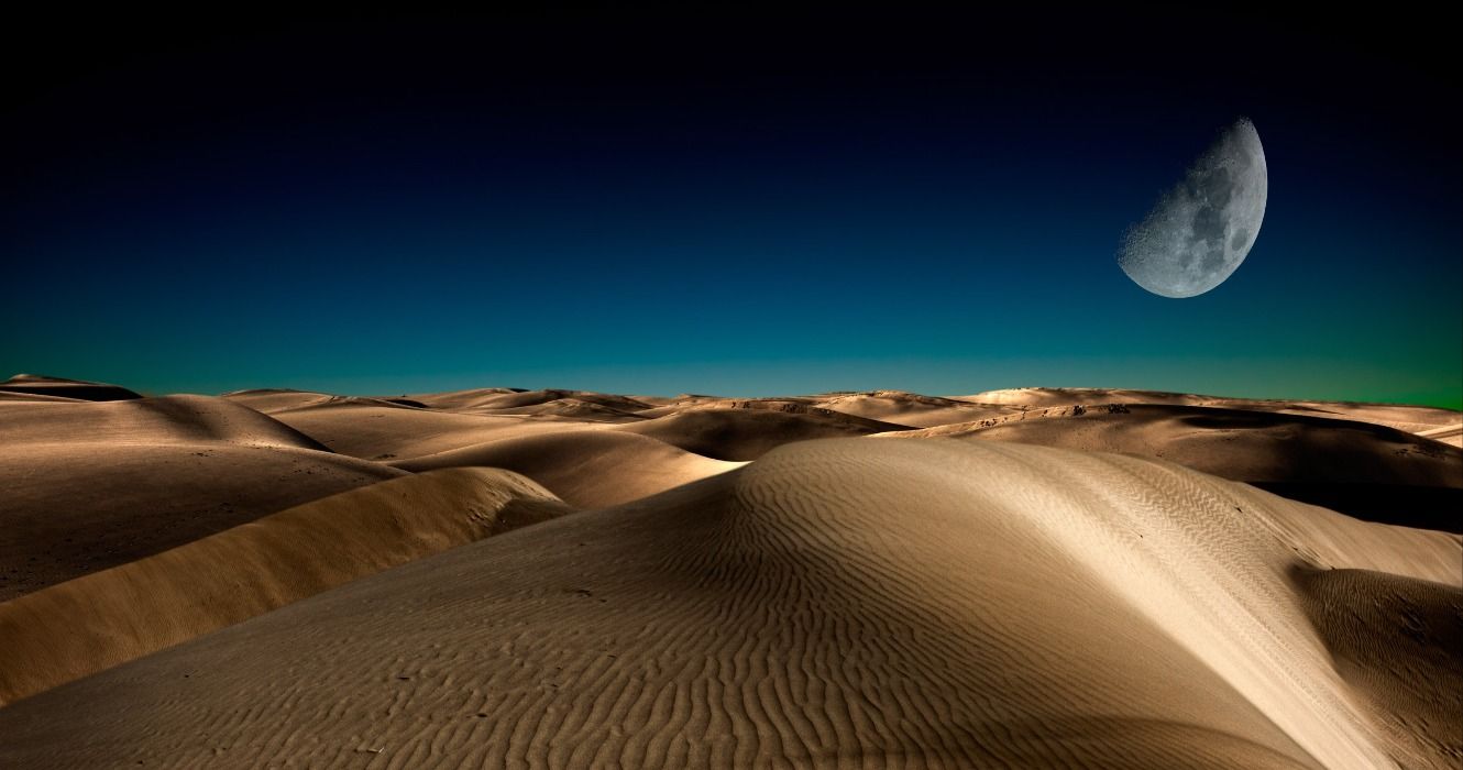 The moon at night over the sand dunes in the Sahara Desert
