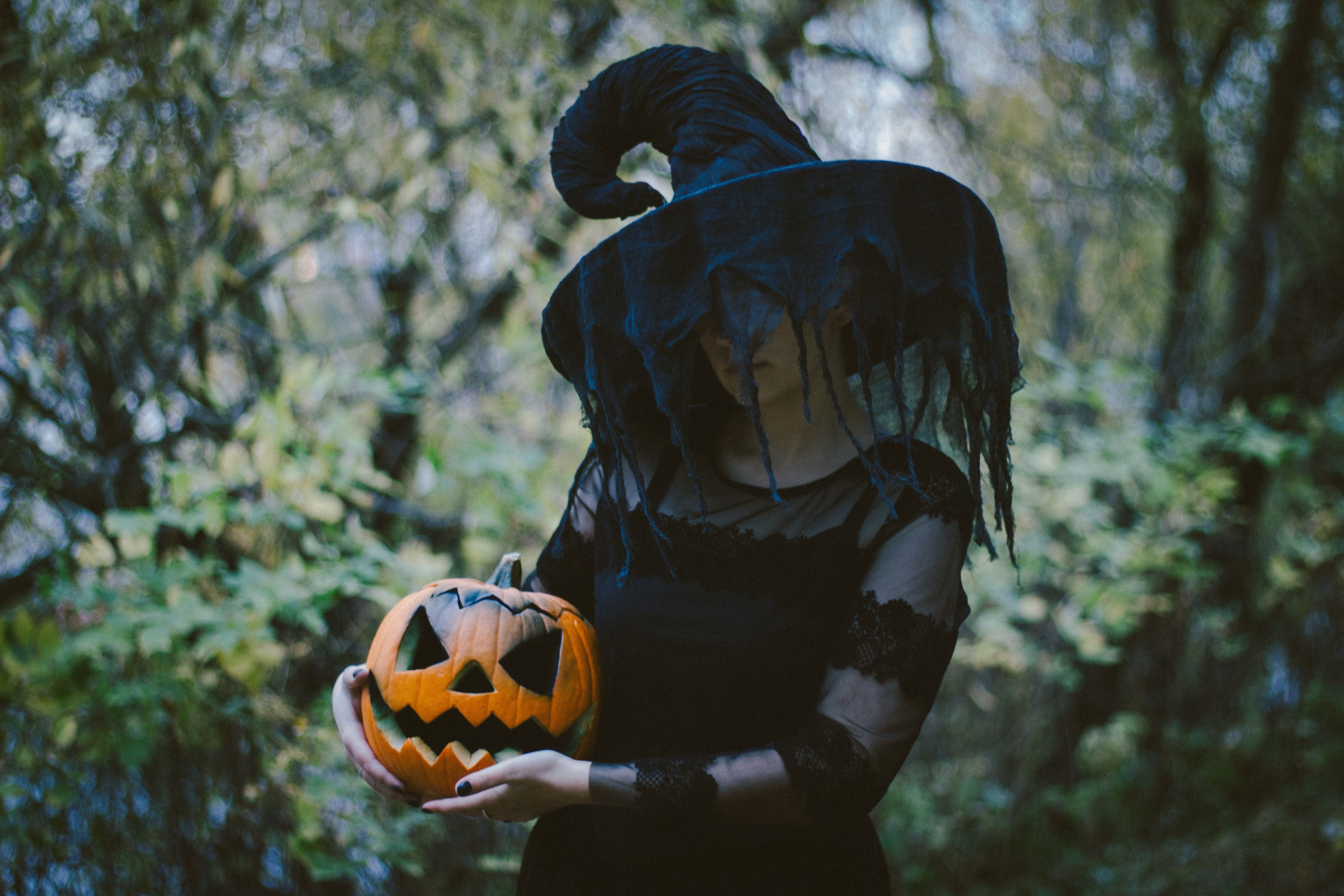 A woman dressed in a witch costume while holding a carved pumpkin for Halloween