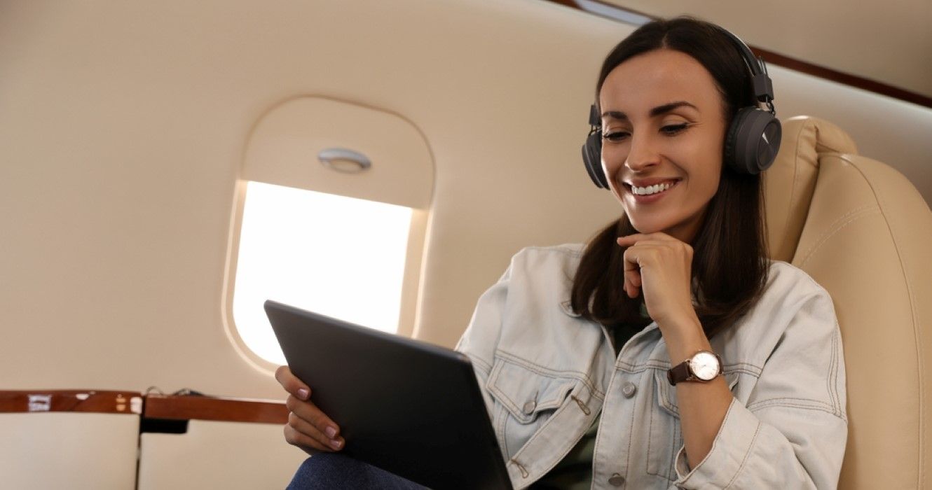 Young woman on airplane with tablet and headphones