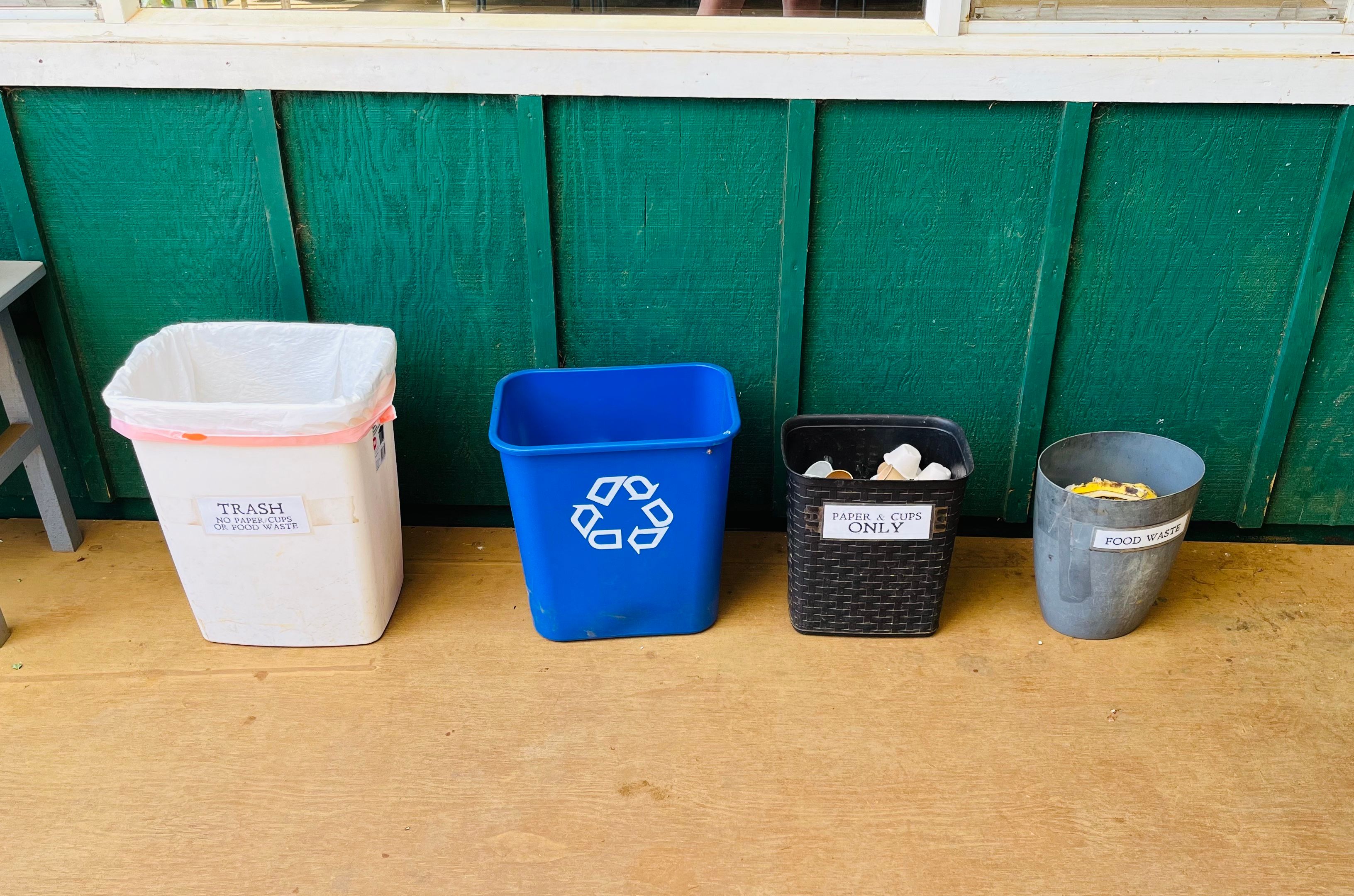 A trash can, blue recycling bin, paper waste, and food waste bin all in a line 