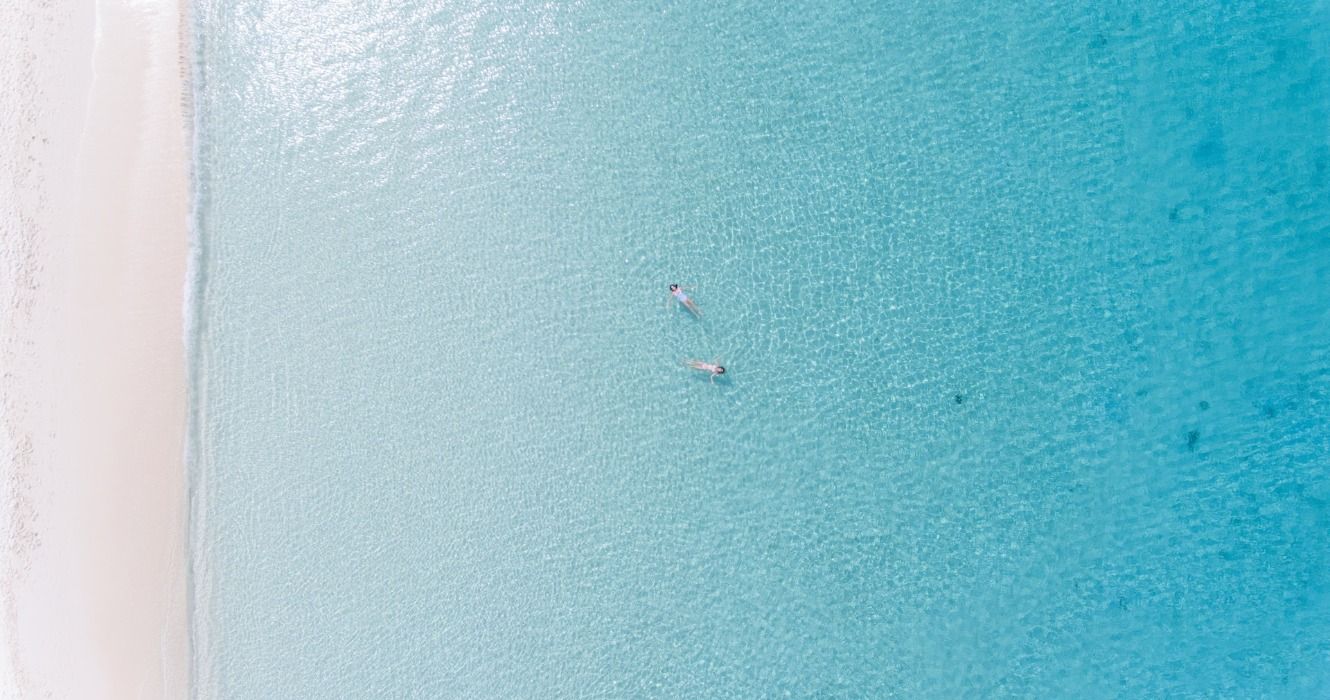 A person floating in the turquoise ocean in the Caribbean Sea off a white-sand beach in Grand Cayman, The Cayman Islands