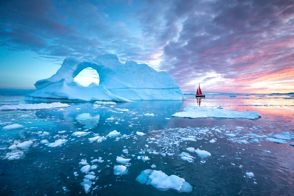 Little red sailboat cruising among floating icebergs in Greenland waters