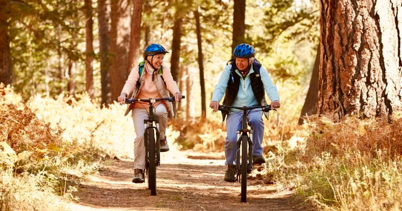 Senior couple mountain biking on forest trail, California