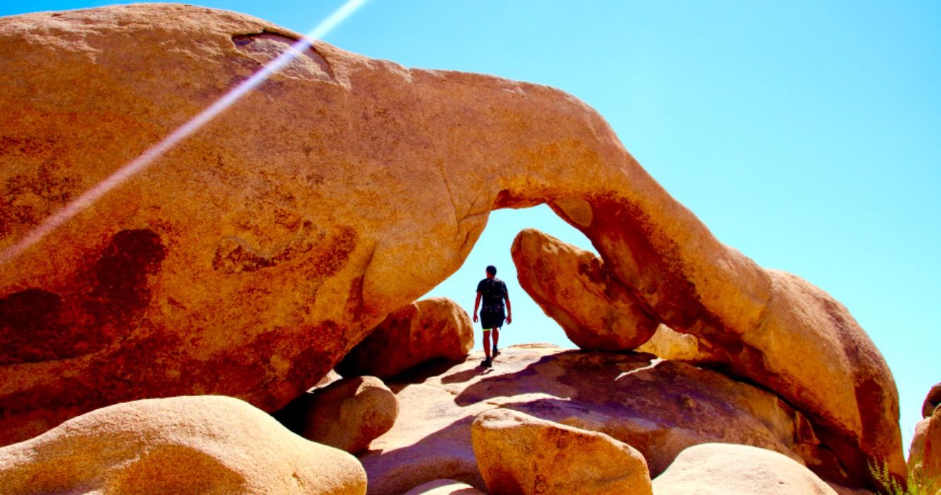 person walking arch rock inside Joshua Tree national park