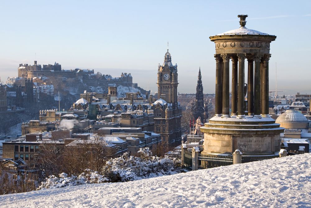 Snow in the winter at Edinburgh City and Castle in Scotland, UK, seen from Calton Hill with the Dugald Stewart monument and Balmoral clock tower