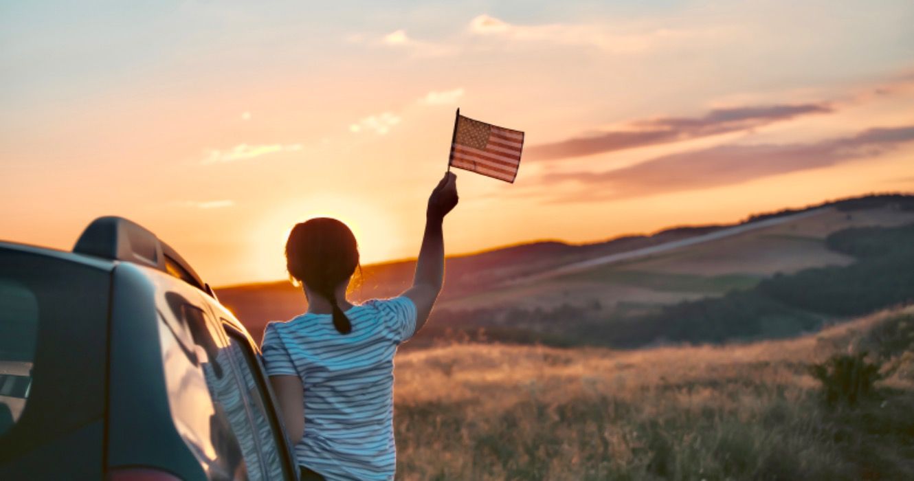 Woman holding an American flag on a road trip. 