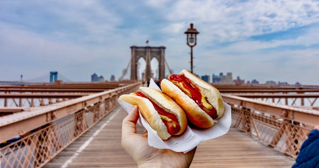 Holding two hot dogs in NYC on the Brooklyn Bridge