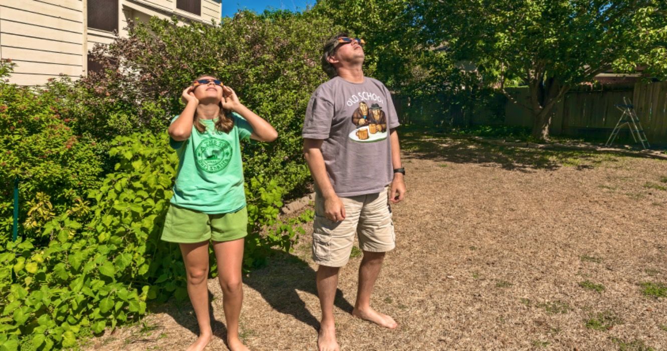 People are watching solar eclipse from their backyard using special glasses.