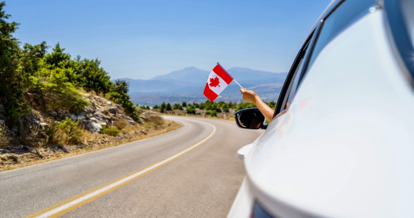 Woman holding Canada flag from the open car window driving along the serpentine road in the mountains. 