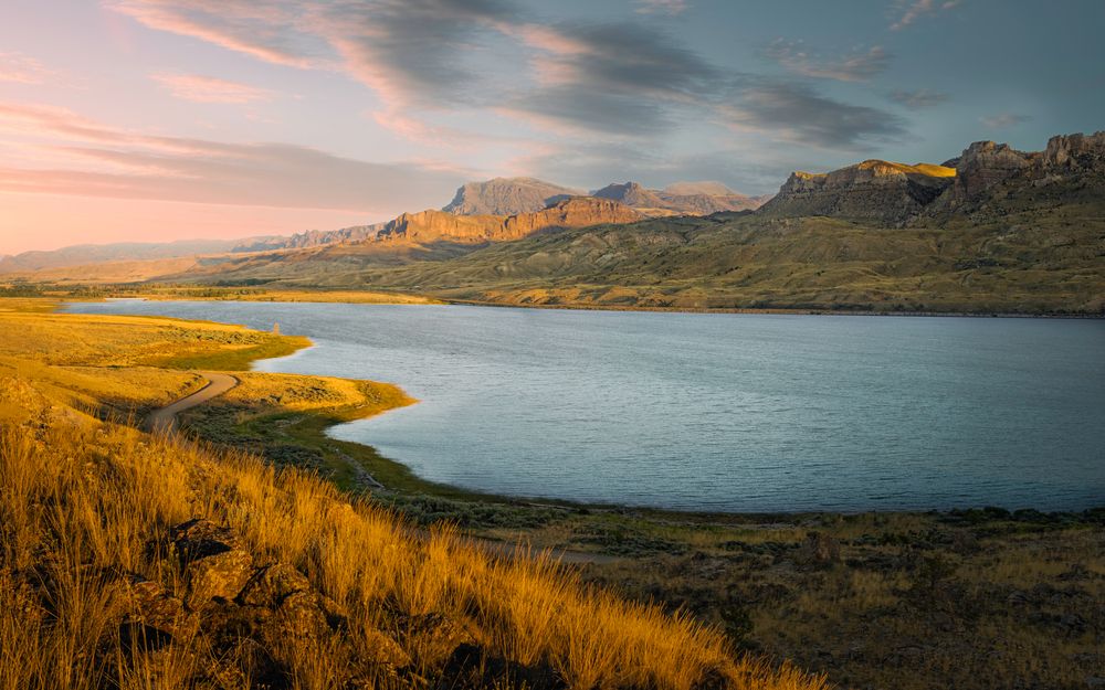 View along Shoshone river with grasses and rocks and foothills of Rocky Mountains on the horizon under colorful sky at dusk near Cody, Wyoming