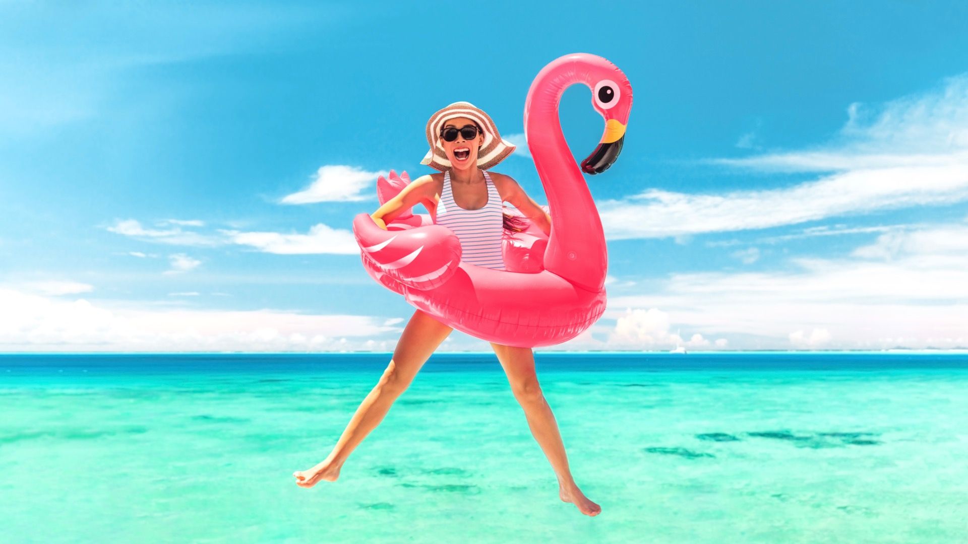 Vacation beach woman jumping of joy with pink flamingo pool float for summer holiday