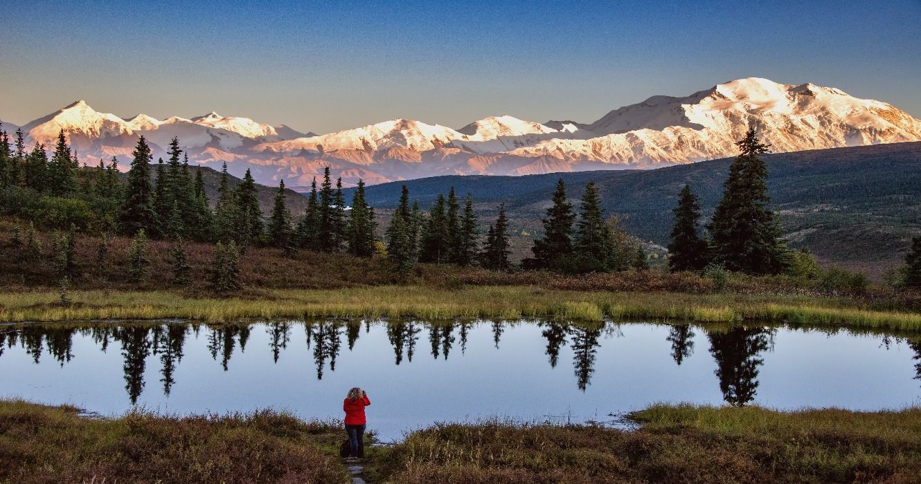 A hiker viewing Mount Denali from a tranquil lake, AK, Alaska, USA