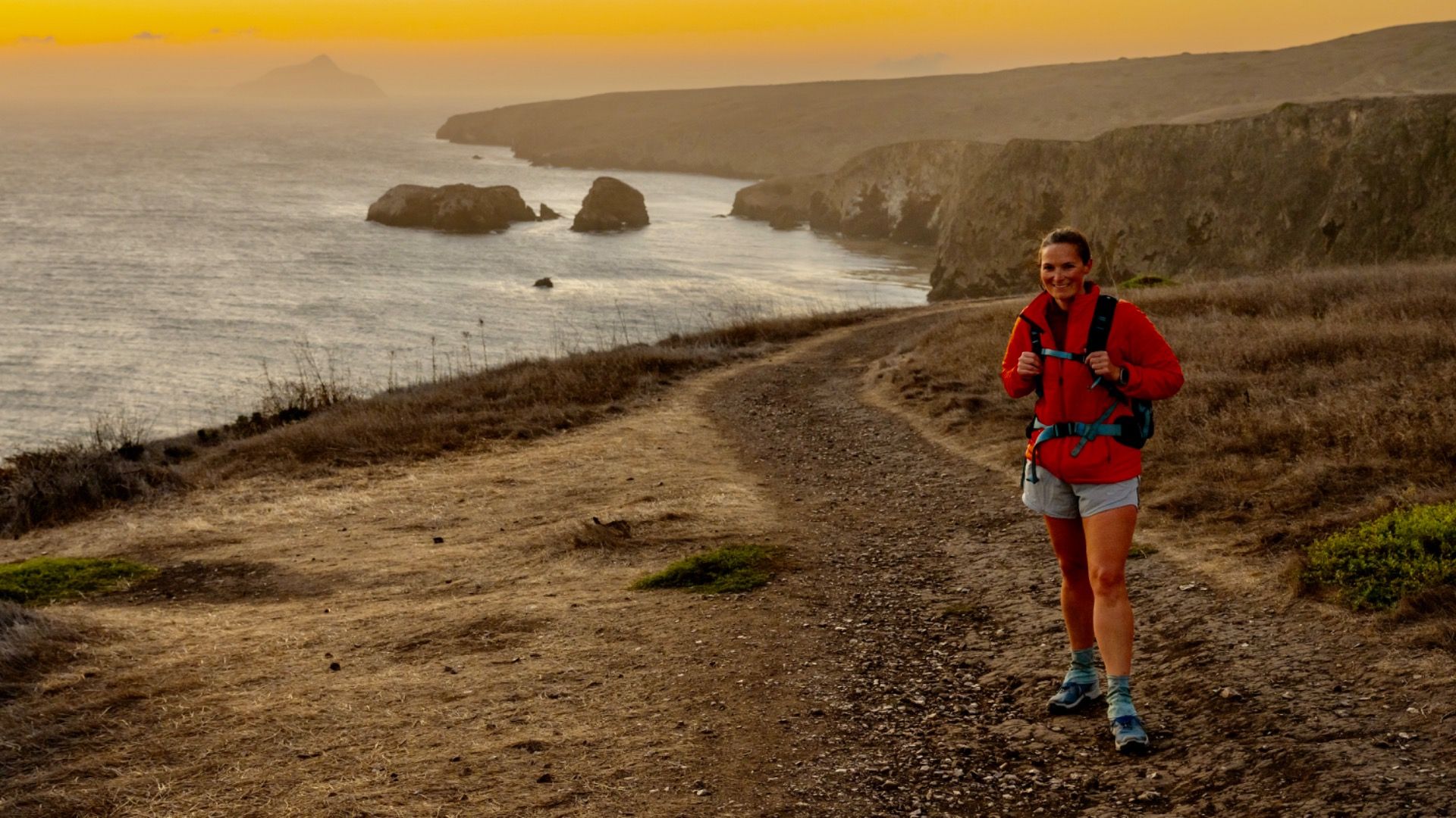 Woman In Orange Coat Stands On Trail Over The Santa Cruz Island Cliffs in Channel Islands National Park