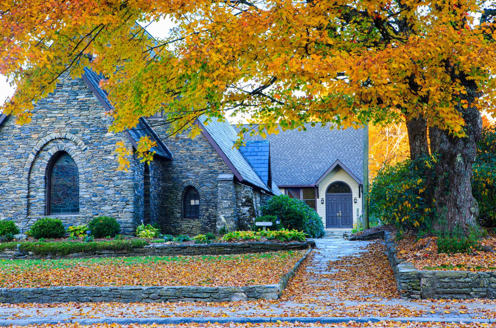 A stone church with orange-colored foliage on the trees and grounds surrounding the building in Blowing Rock, North Carolina