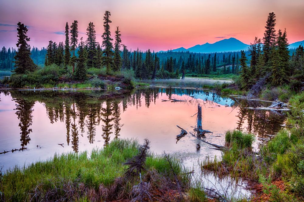 A smoky haze hangs over the distant mountains as the sun sets over a lake in Wrangell-St Elias National Park, Alaska