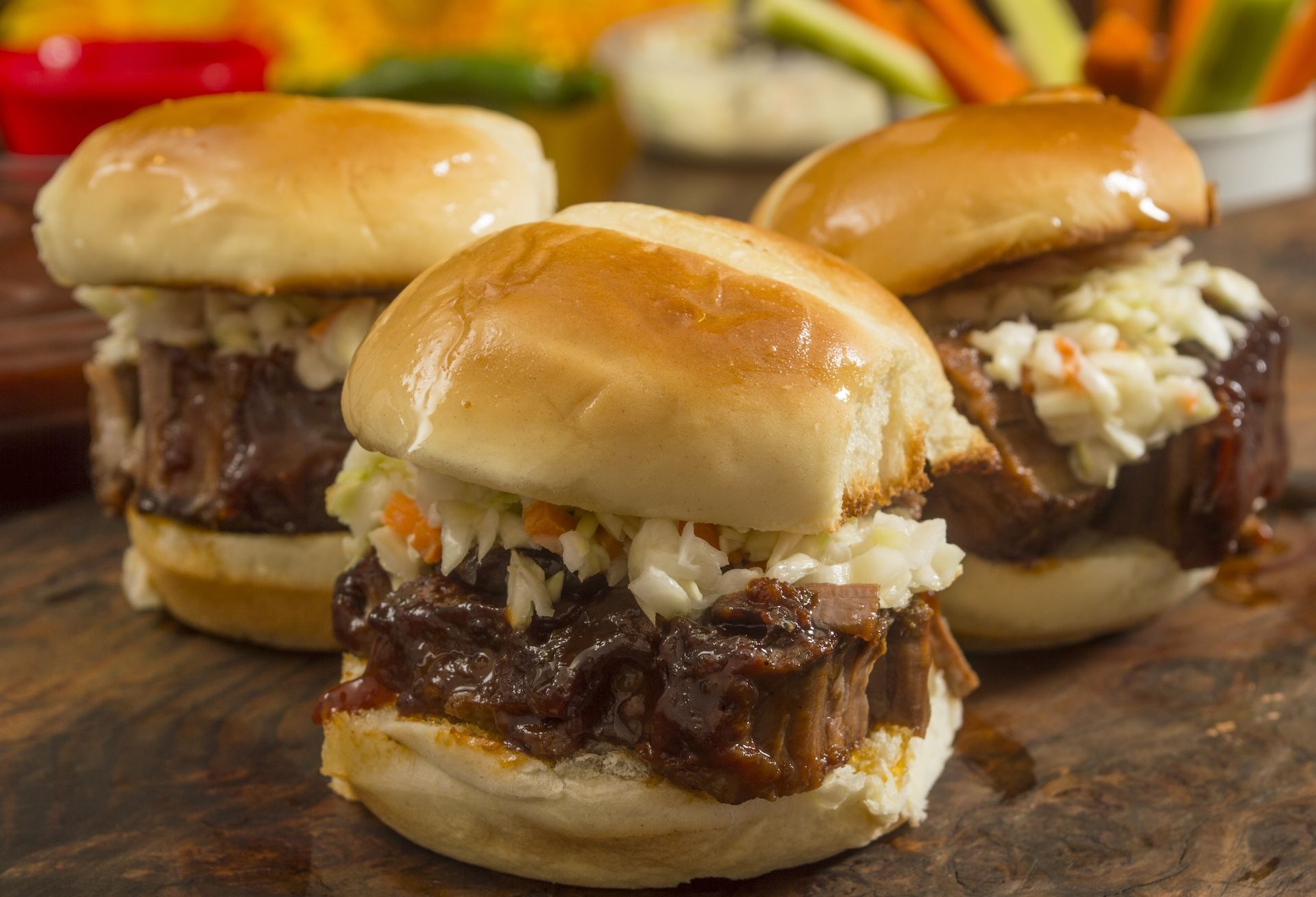 Three brisket sandwich sliders with tender meat, topped with sauce and served on soft buns.